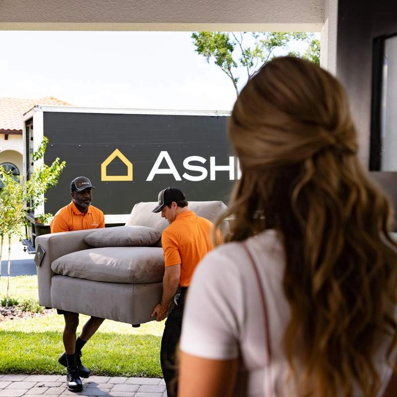 person watching 2 Ashley delivery experts delivering new Ashley Furniture